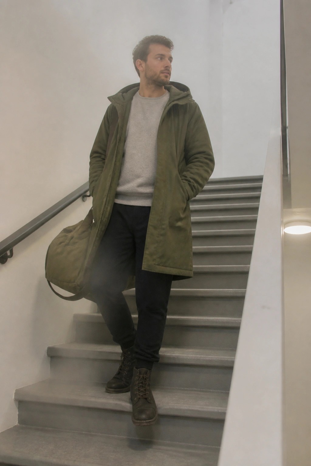 Man in olive parka with duffel bag on grey indoor staircase