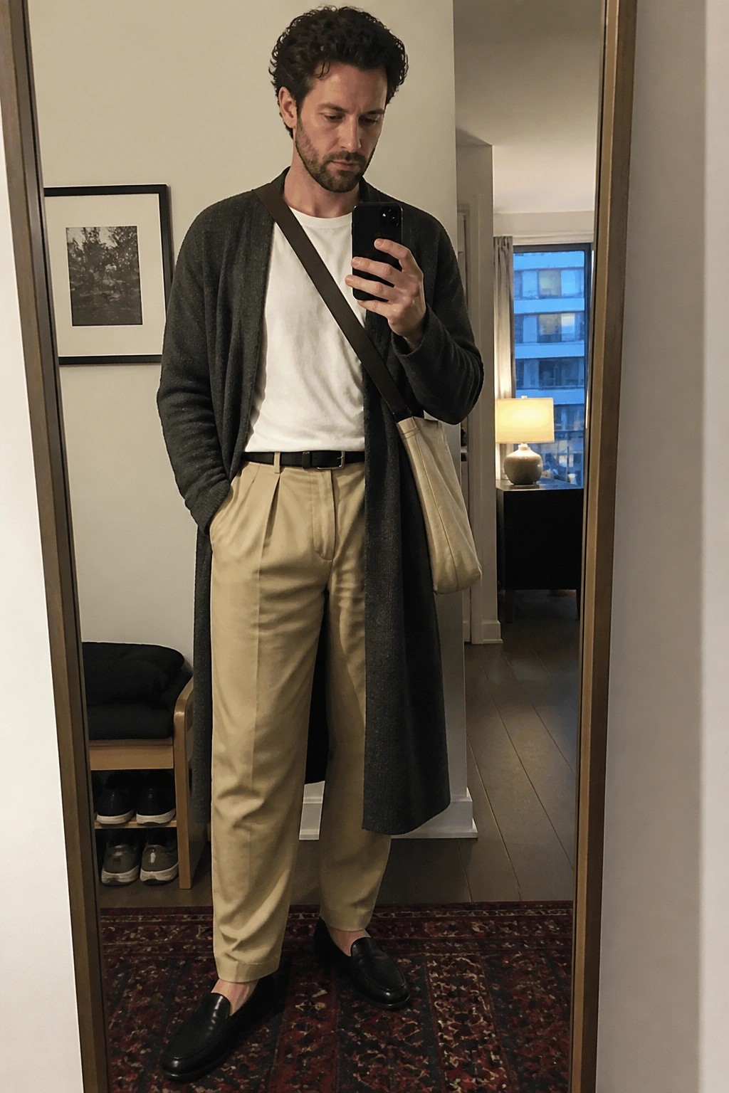 Bearded man in gray cardigan, white tee, beige pants, black loafers, with beige tote bag.