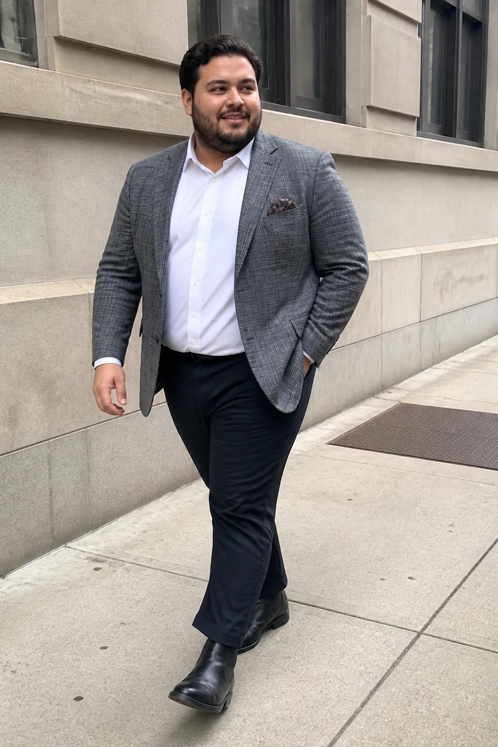 Man in gray plaid blazer and white shirt stands on city sidewalk