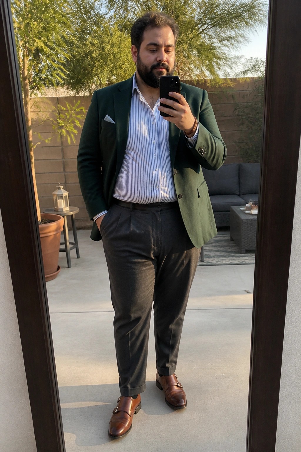 Man wearing dark green blazer over light blue striped shirt with gray trousers and brown double monk strap shoes taking a mirror selfie