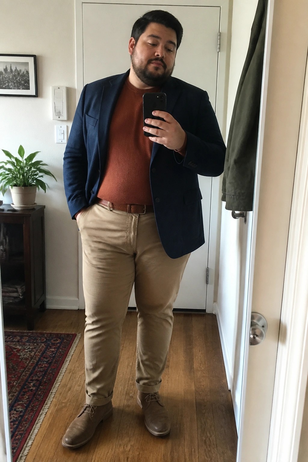 Man taking mirror selfie in navy blazer, rust sweater, khaki pants, and brown shoes