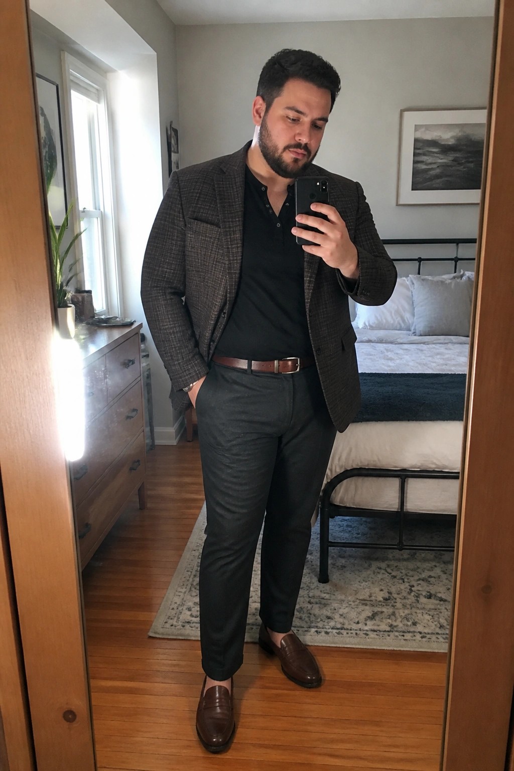 Man in plaid blazer and black shirt taking mirror selfie in bedroom