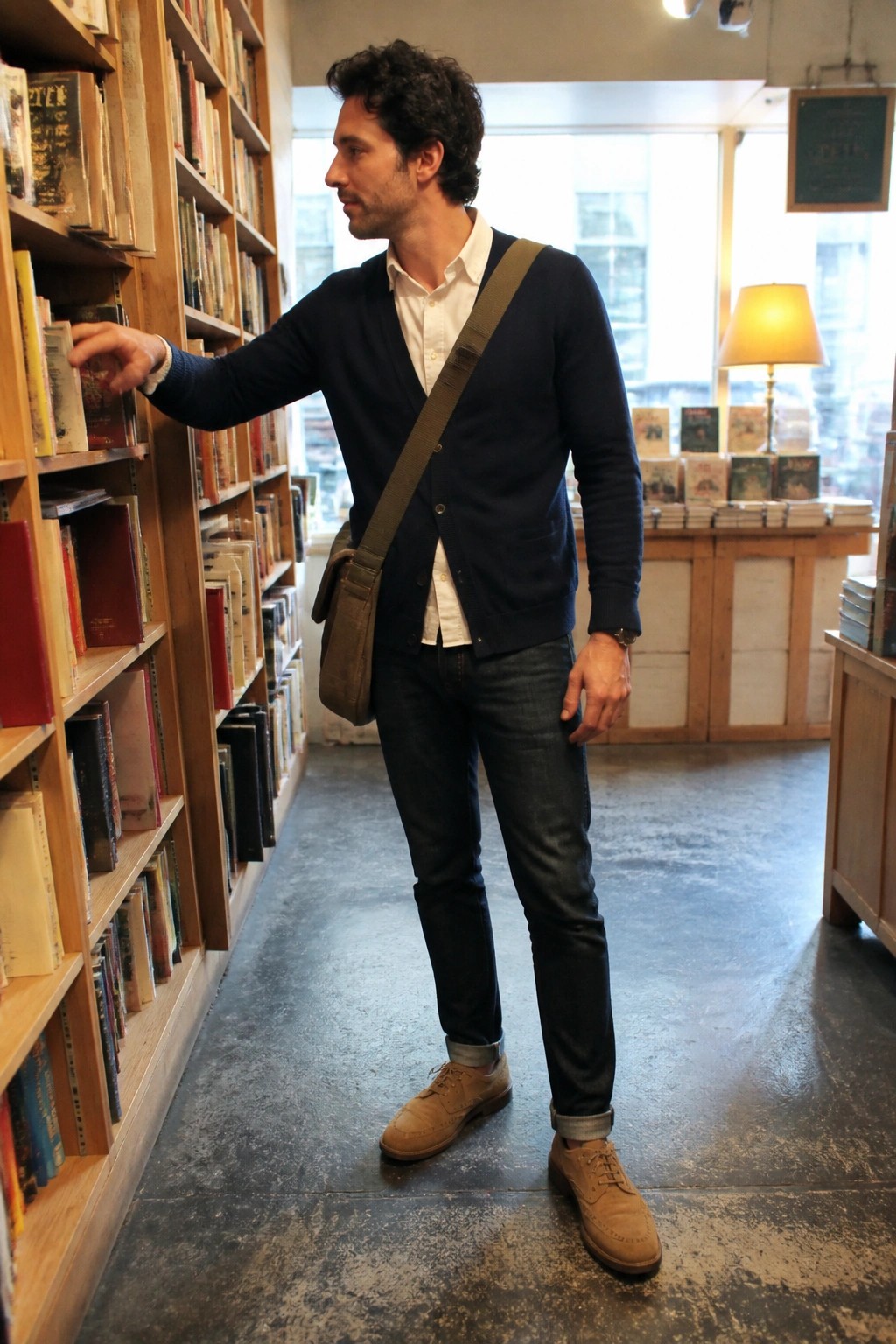 Man in navy cardigan reaches for book on wooden bookshelf in store