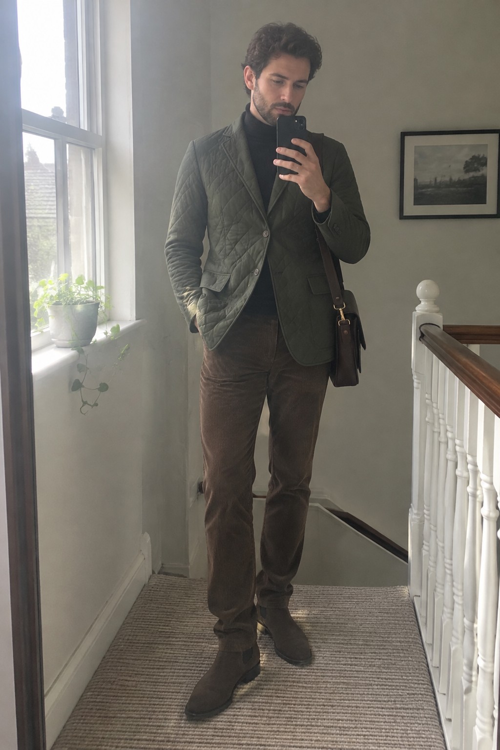 Man wearing an olive quilted blazer over a black turtleneck with brown corduroy trousers, brown suede ankle boots, and a dark leather crossbody bag.