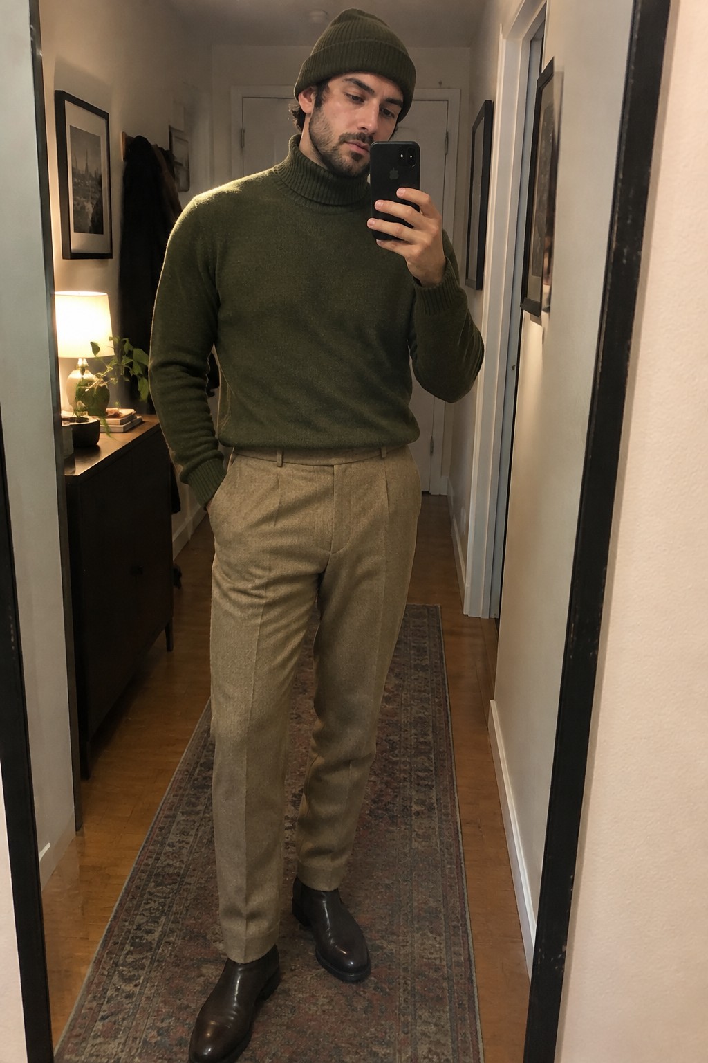 Man wearing an olive turtleneck sweater and matching beanie with light brown pleated trousers and dark brown Chelsea boots.