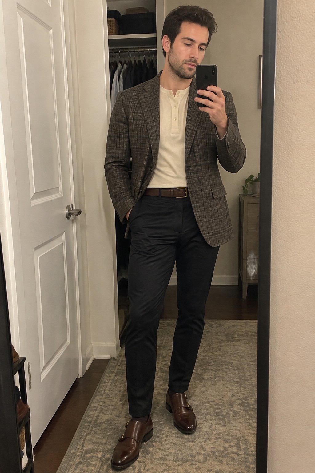 Man wearing a brown plaid blazer over a cream henley, black trousers, a brown belt, and brown leather double monk-strap shoes.