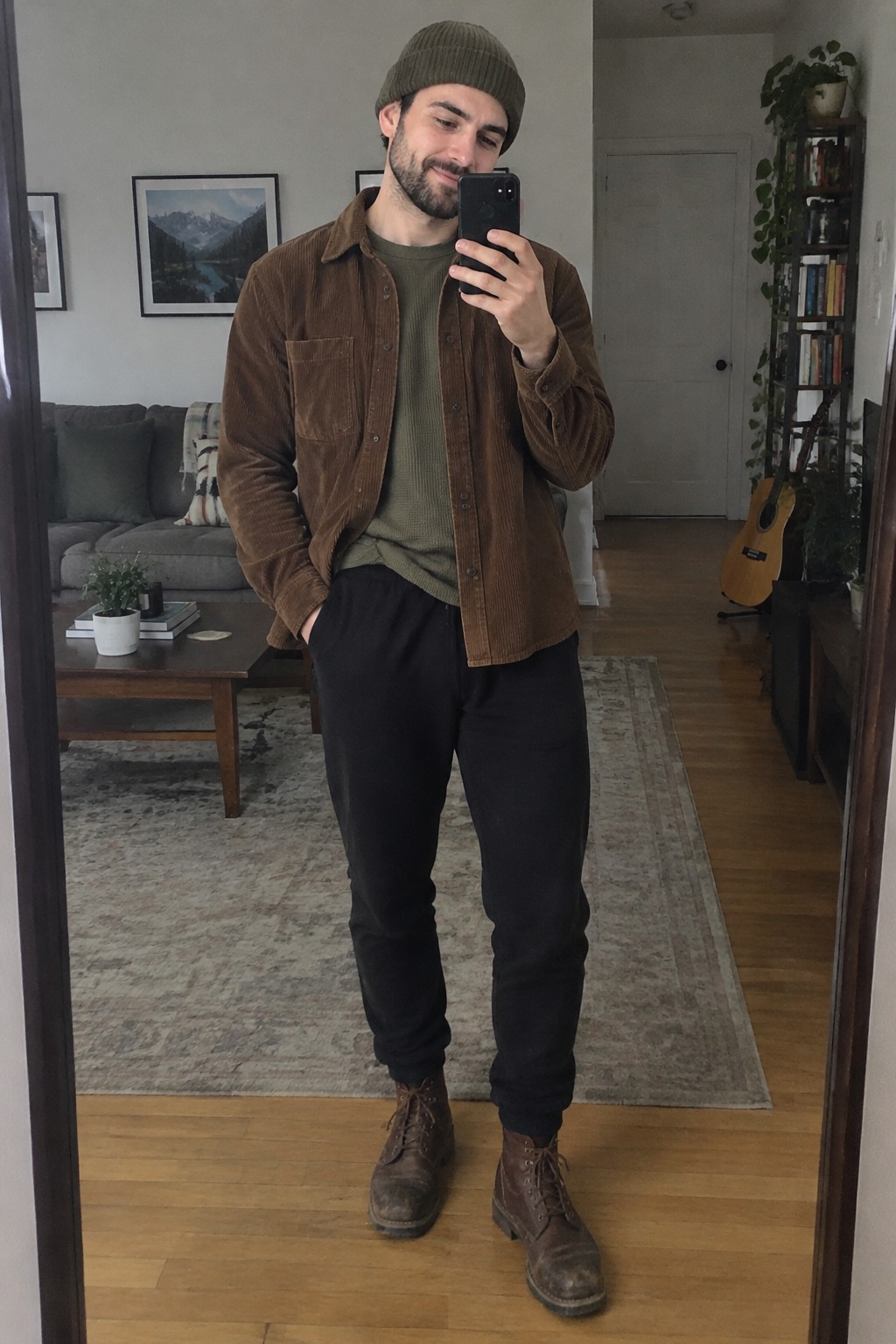 Man wearing an olive knit shirt, brown corduroy overshirt, dark trousers, brown lace-up boots, and an olive-brown beanie.
