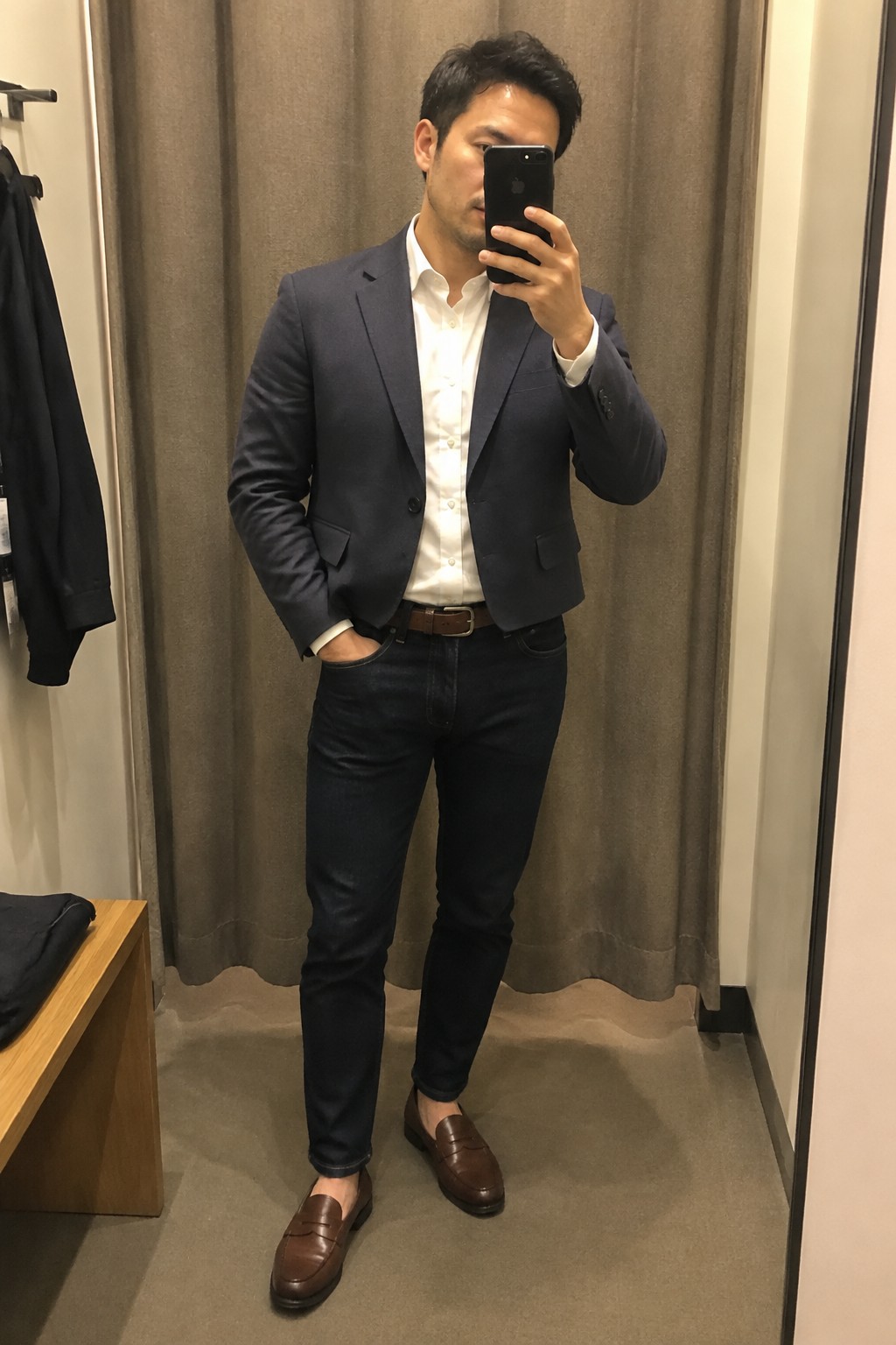 A man wearing a navy blazer over a white shirt, dark jeans, a brown belt, and brown leather loafers.