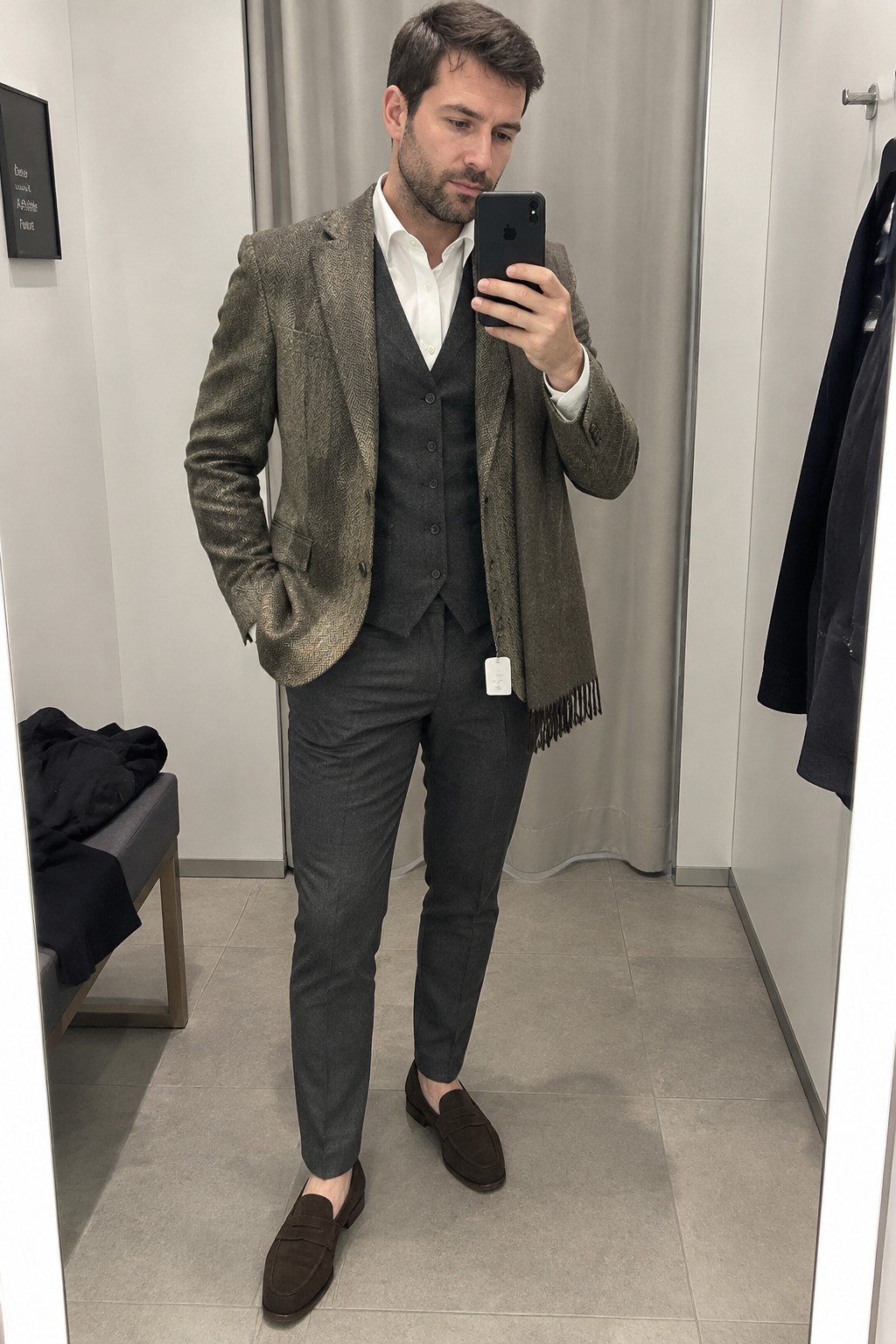 Man wearing an olive-brown tweed blazer over a charcoal waistcoat, white shirt and charcoal trousers, with a brown scarf and dark brown suede loafers.