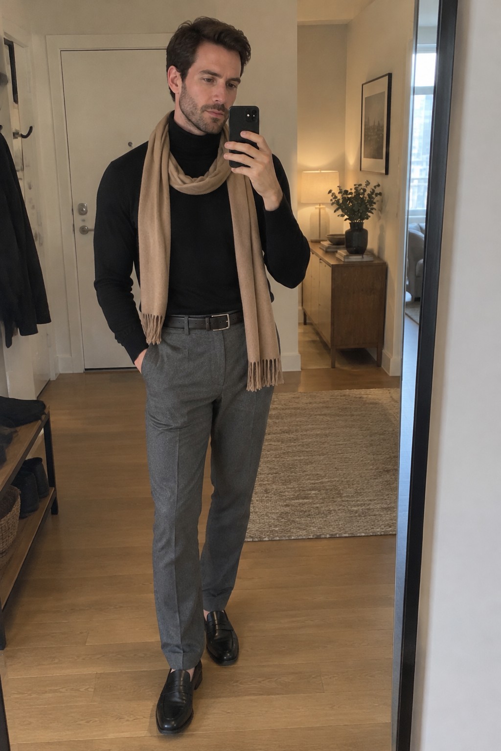 Man wearing a black turtleneck, camel scarf, gray tailored trousers, black belt, and black leather loafers.