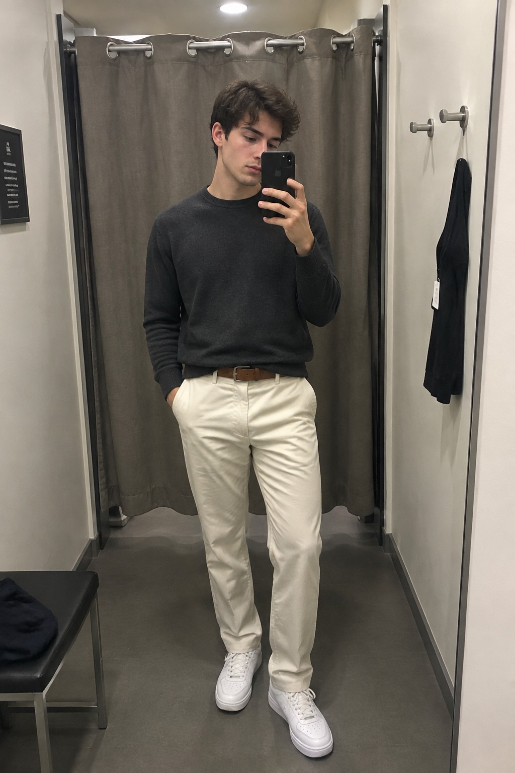 Man wearing a charcoal crewneck sweater tucked into cream straight-leg trousers with a brown leather belt and white sneakers.