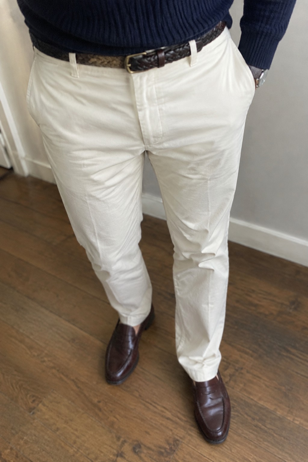 Man wearing a navy ribbed sweater, cream straight-leg trousers, a dark woven brown belt, and burgundy leather loafers.