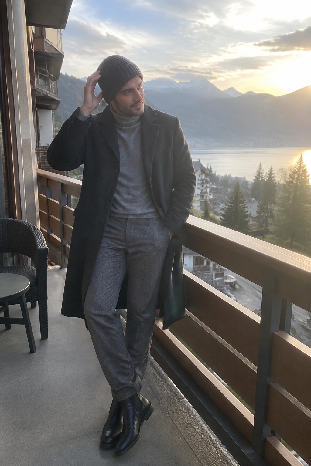 A man wearing a long black overcoat, grey turtleneck sweater and wool trousers, black ribbed beanie, and black Chelsea boots.