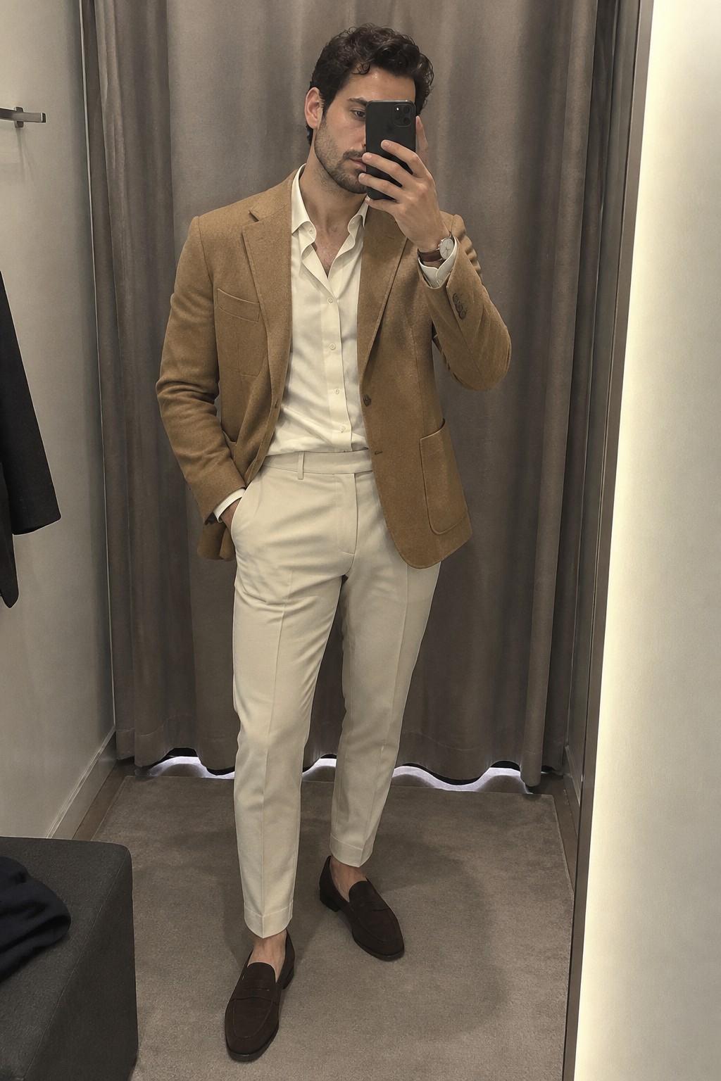 Man wearing a camel blazer, open-collar white shirt, cream trousers, dark brown loafers, and a wristwatch.