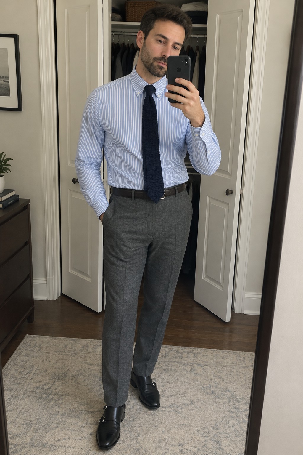 Man wearing a blue-and-white striped Oxford shirt, navy tie, charcoal-gray trousers, dark belt, and black monk-strap shoes.